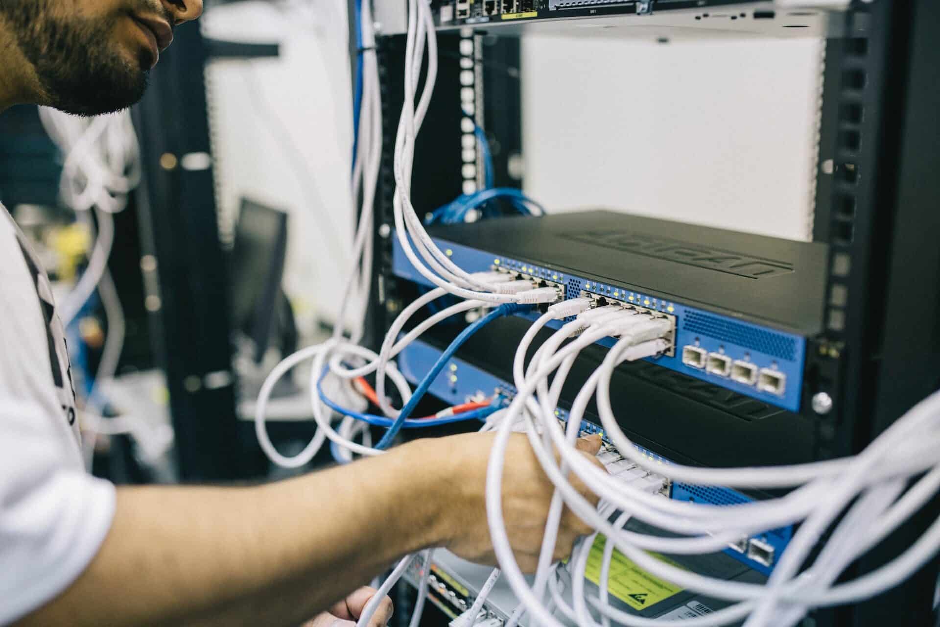 A man plugging Ethernet cords into a network switch in a rack